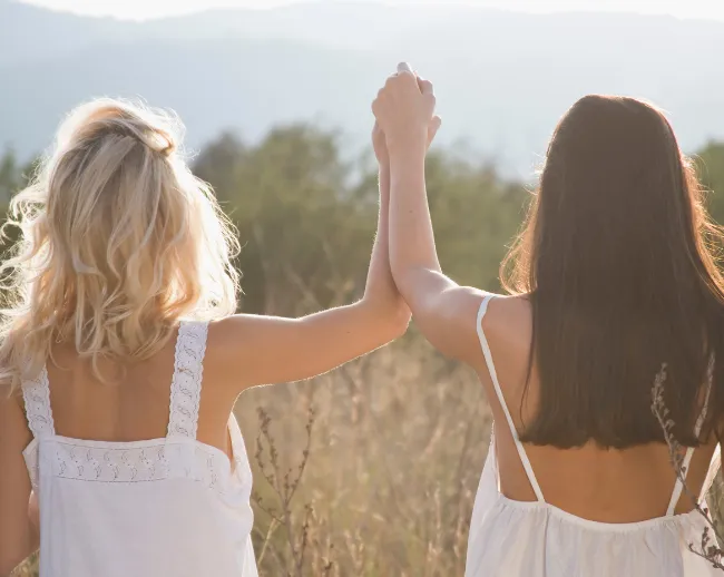 Zwei Frauen gehen Hand in Hand durch eine Sommerwiese