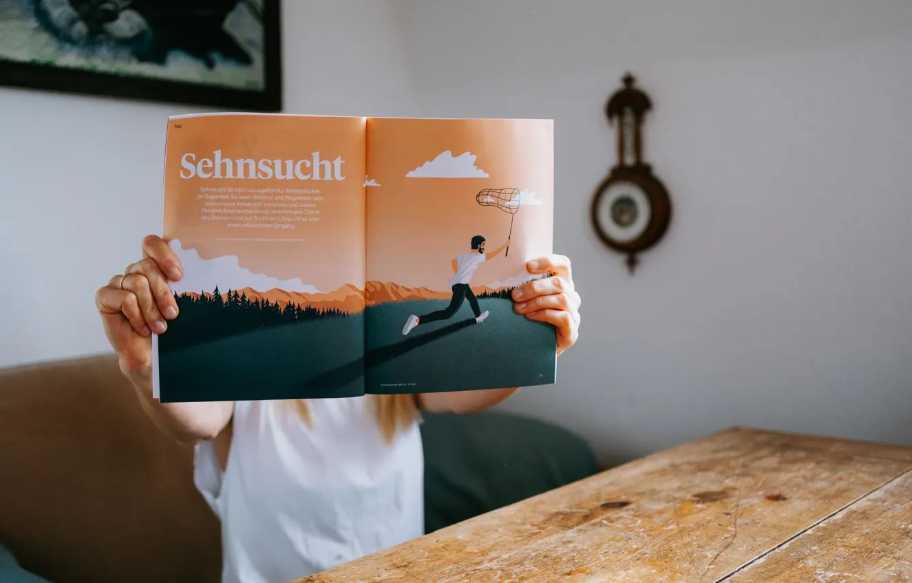 Eine Person hält ein aufgeschlagenes Magazin mit der Überschrift „Sehnsucht“